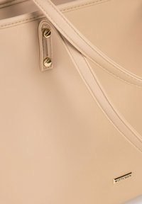 Borsa a tracolla sintetica beige con hardware dorato, doppio manico e una texture liscia con un discreto dettaglio del logo.