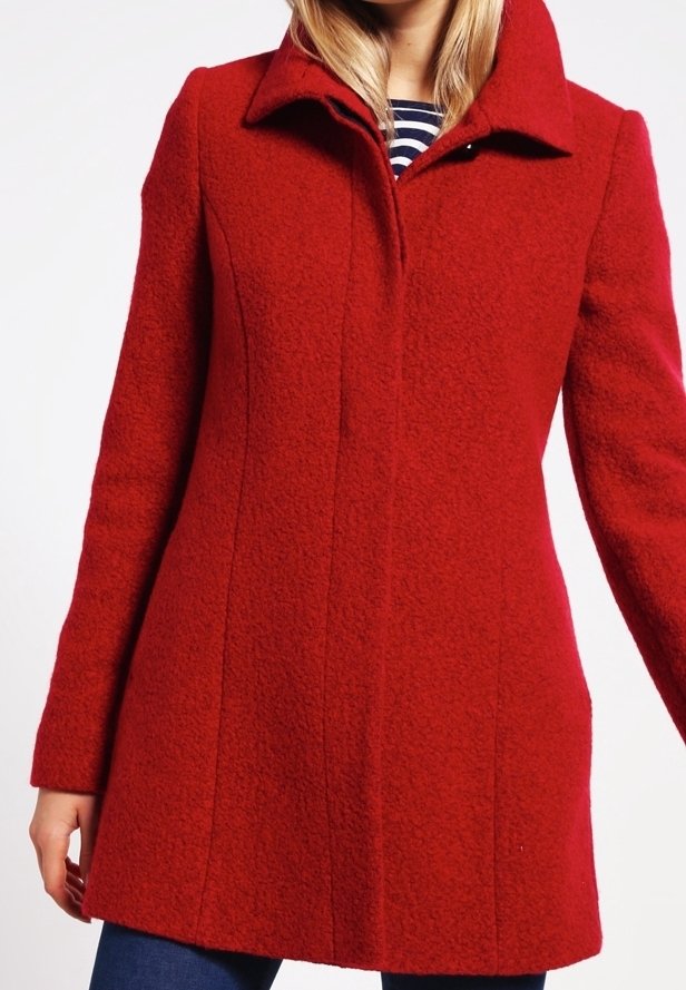 Femme portant un manteau rouge en laine texturée, sur mesure, avec un large col, par-dessus un haut rayé bleu marine et blanc.