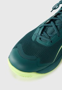 Teal träningssko med texturerad mesh-överdel, gröna detaljer och gummisula. Har rund tå och snörningssystem för en säker passform.