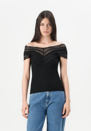 Svart av- skulder topp med blonderte detaljer og ribbet tekstur. Har en V-formet halslinje og korte ermer, kombinert med lyseblå jeans.