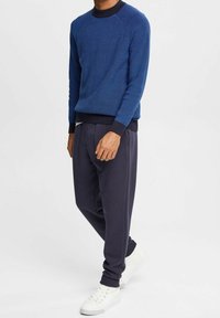 Blå texturerad crewneck-tröja med mörk ribbad halsringning, tillsammans med mörkgrå avslappnade byxor och vita sneakers.