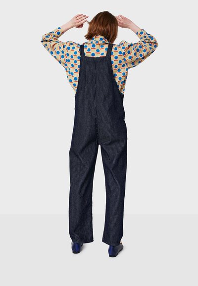 Blue and white striped overalls with wide legs, adjustable straps, and side pockets, worn over a patterned long-sleeve shirt.