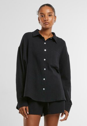 Black cotton blend button-up shirt with a relaxed fit, textured surface, long sleeves, and a single chest pocket. Features white buttons.