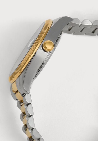 Vue latérale d'une montre-bracelet argent et or avec une lunette et une couronne dorées striées, et un bracelet métallique bicolore à maillons.