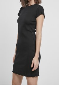 Schwarzes, geripptes Kleid mit kurzen Ärmeln, rundem Ausschnitt und ausgefranstem Saum. Hergestellt aus strukturiertem Stoff, figurbetonte Silhouette.