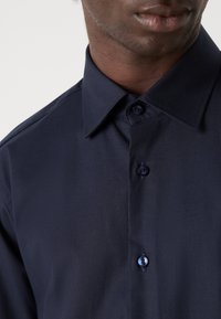 Camisa azul marino de botones fabricada en un tejido texturizado, con un cuello puntiagudo y botones a juego con un patrón sutil.