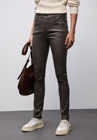 Pantalones ajustados de color marrón oscuro hechos de una tela suave, con bolsillos frontales y cremallera, combinados con un bolso de ante marrón y zapatillas blancas.