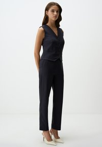 Marineblauwe gestreepte vest met een diepe V-hals, drie knopen sluiting, gecombineerd met bijpassende slim-fit broeken en witte puntige hakken.