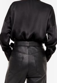Camicia nera in satin con una vestibilità ampia e maniche lunghe, abbinata a pantaloni in pelle nera a vita alta con una texture liscia e tasche posteriori.