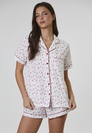 Korte mouwen pyjamaset van witte stof met rode kersenprint, voorzien van een zakje, rode bies en bijpassende korte broek met elastische tailleband.