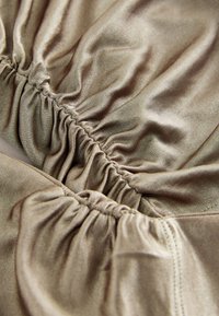 Zeltaini mirdzoša auduma ar vieglu spīdumu, ar sasietām daļām un gludu tekstūru. Dizainā ir ietvertas elastīgas kroku apmales pa malām.