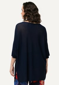 Marineblaue, oversized Tunika mit kurzen Ärmeln, leichtem Stoff, seitlichen Schlitzen und weiter Ausschnitt, kombiniert mit gemusterten Hosen.