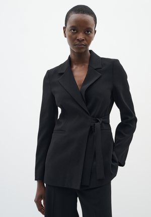Black tailored blazer with a wrap design, notched lapels, and long sleeves. Features a tied waist and side pockets. Smooth fabric texture.