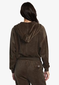 Felpa ampia in velluto marrone con cappuccio, caratterizzata da polsini e orlo a coste, progettata con un pantalone coordinato e un piccolo logo.