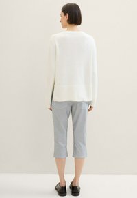 Weißer Strickpullover mit geripptem Saum, kombiniert mit hellblauen verkürzten Hosen. Schwarze Schuhe runden das Outfit ab. Strukturiertes Gewebe sichtbar.