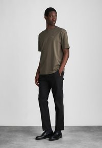 Olijfgroene t-shirt met korte mouwen en ronde hals, gecombineerd met zwarte op maat gemaakte broek en zwarte instappers. Glad materiaal, eenvoudig ontwerp.