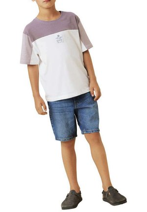 T-shirt blanc et lavande à manches courtes avec une étiquette à l'avant, associé à un short en denim bleu de longueur genou et des chaussures gris à enfiler.
