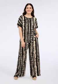Top de tie-dye en negro y beige con mangas cortas, combinado con pantalones de pierna ancha. Ambas prendas están confeccionadas con una tela suave y lisa.
