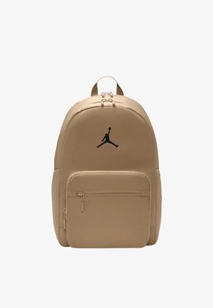 Zaino beige con superficie in tessuto liscia, caratterizzato da una tasca frontale con cerniera e un logo Jumpman nero. Spallacci doppi regolabili.