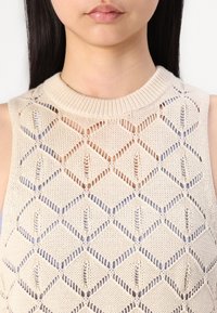 Top senza maniche lavorato a maglia con un motivo a diamante, realizzato in filato beige chiaro con un design a maglia aperta e dettagli a costine sul collo.