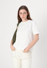 Hvid bomulds t-shirt med rund hals, korte ærmer og et lille logo. Sammen med lysebeige jeans med kontrastsyninger og lommer.