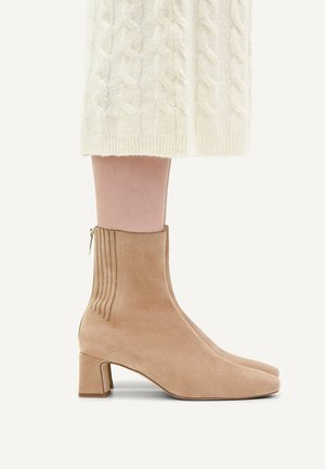 Light brown suede ankle boots with block heels worn with a cream cable-knit skirt visible from mid-calf down.