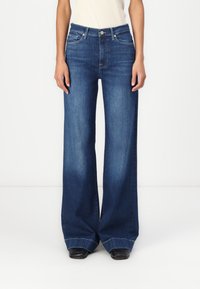 Videben bukse i mørk blå denim, med høy midje, fem lommer og rå kant. Materialet har en glatt tekstur.