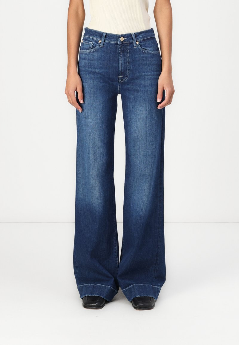 Videben bukse i mørk blå denim, med høy midje, fem lommer og rå kant. Materialet har en glatt tekstur.
