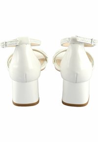White patent leather high heels with a chunky heel, ankle straps, and decorative glitter accents on the strap. Smooth surface and rounded shape.
