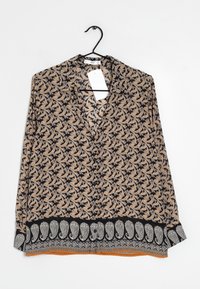 Blouse à manches longues avec un motif paisley orange et blanc sur fond noir, dotée d'un décolleté en V et d'un détail de ourlet orné.