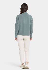 Fleece pullover in zacht, textuur lichtblauw met een hoge kraag; gecombineerd met licht crèmekleurige broek en neutrale sneakers. Ontspannen pasvorm en lange mouwen.