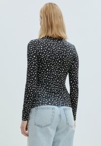 Zwarte lange mouwen top met een wit abstract patroon, aansluitend ontwerp en een ronde halslijn. Gecombineerd met lichtblauwe high-waisted jeans.