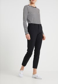 Černé slim-fit kalhoty s opaskem v pase, spárované s dlouhým rukávem černobíle pruhovaným topem a bílými teniskami.