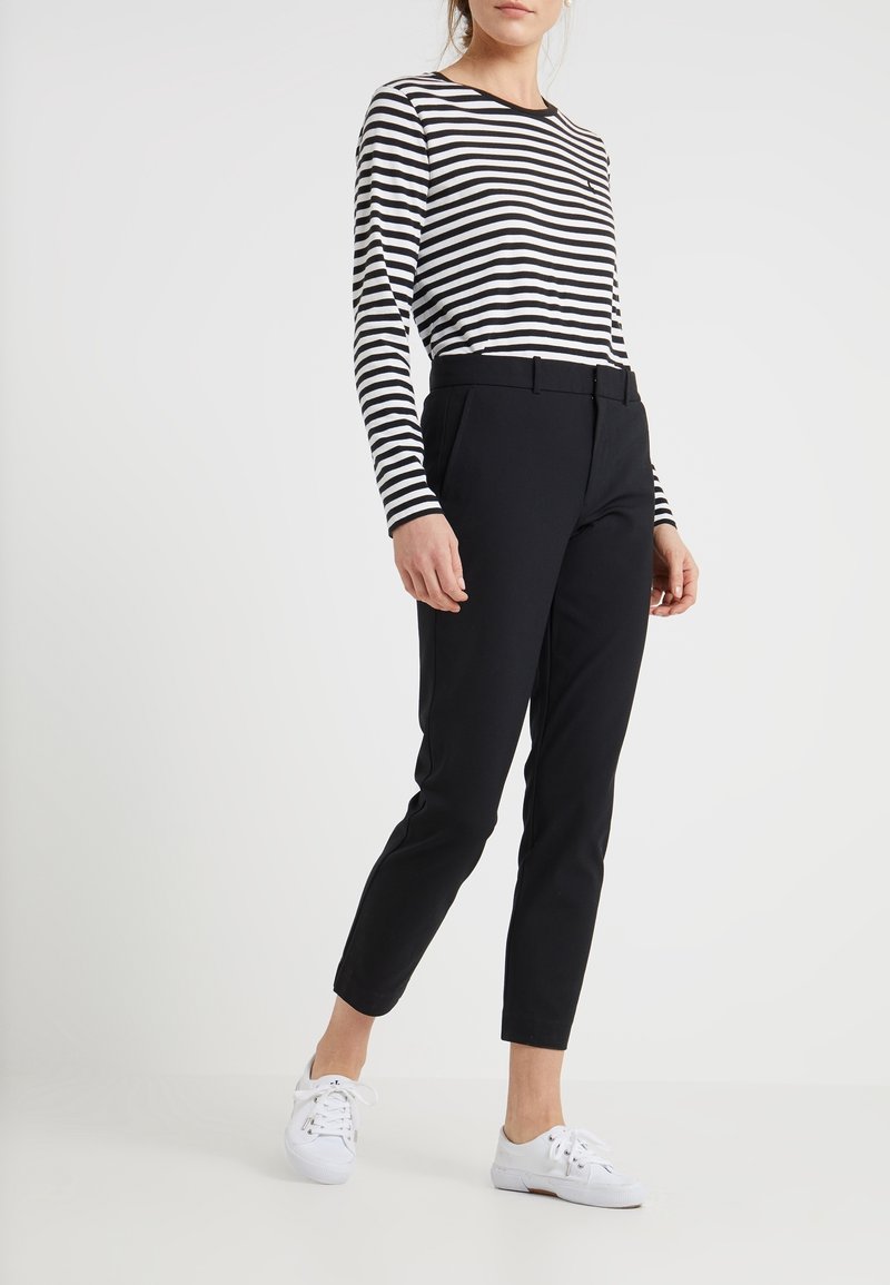 Černé slim-fit kalhoty s opaskem v pase, spárované s dlouhým rukávem černobíle pruhovaným topem a bílými teniskami.
