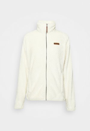 Bijela flis jakna s visokim ovratnikom, prednjim patentnim zatvaračem, teksturiranom vanjskom površinom i smešnim logom na lijevoj strani grudi.