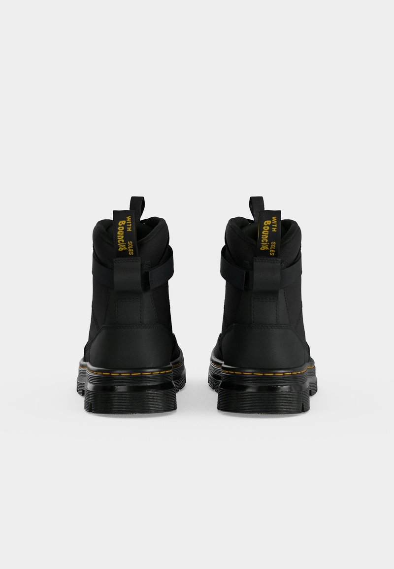 Pair of black ankle boots with pull tabs and yellow stitching on thick soles, shown from the back against a plain background.