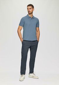 Jasnoniebieska koszulka polo z krótkim rękawem i kołnierzykiem, w połączeniu z ciemnoszarymi spodniami slim-fit i kremowymi trampkami. Prosty design, minimalne akcenty.