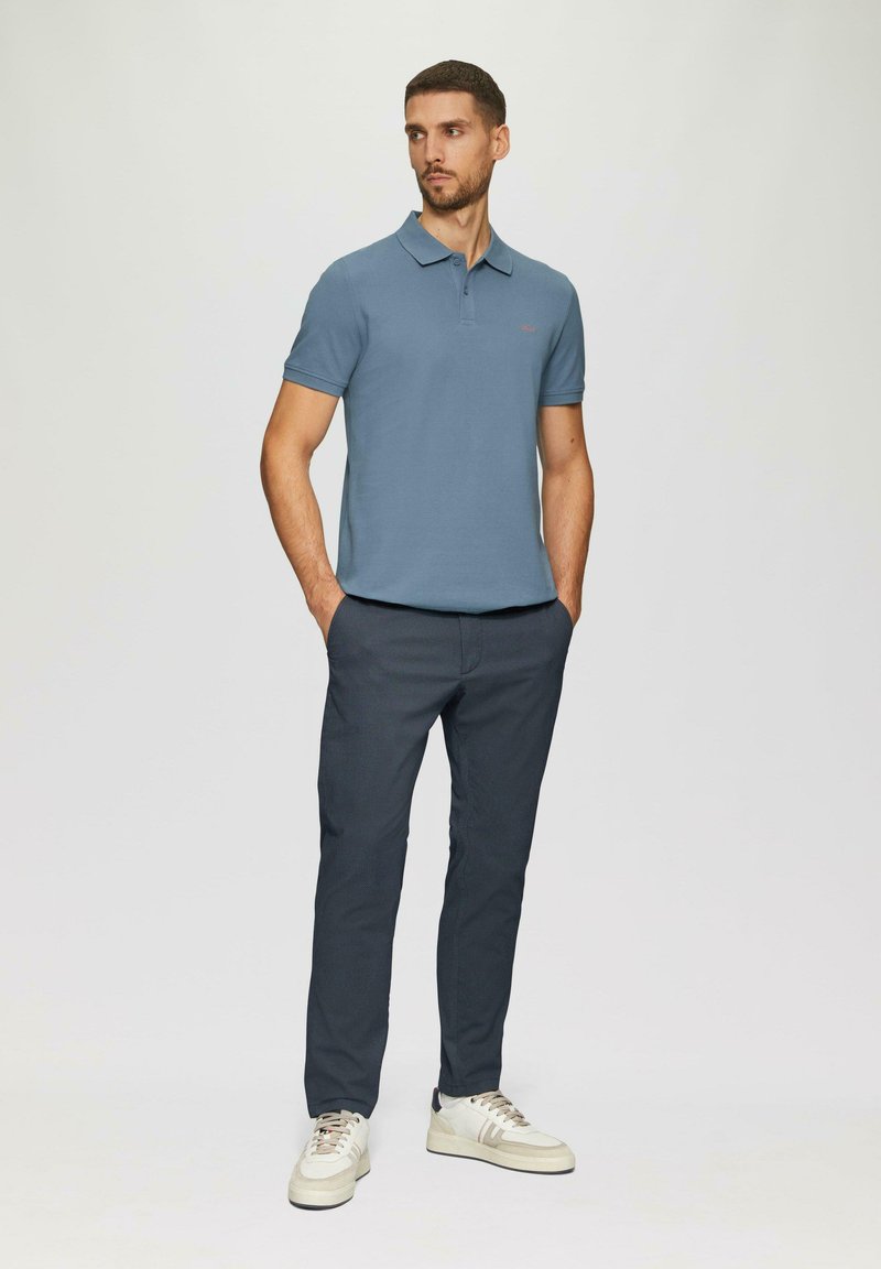 Jasnoniebieska koszulka polo z krótkim rękawem i kołnierzykiem, w połączeniu z ciemnoszarymi spodniami slim-fit i kremowymi trampkami. Prosty design, minimalne akcenty.