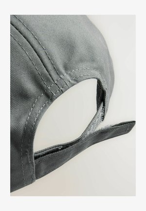 Grå basebollkeps med en texturerad tygkvalitet. Har en justerbar rem i ett liknande material, med synliga sömmar som detalj.