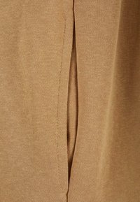 Gros plan d’un tissu tricoté beige montrant une fente latérale verticale avec des coutures visibles le long des bords.