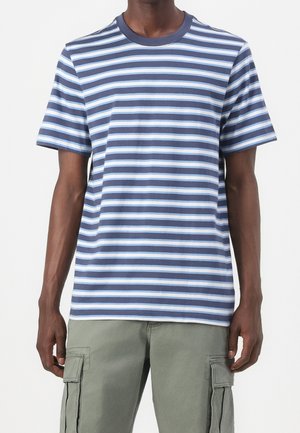 Man wearing a blue and white striped short-sleeve t-shirt paired with light gray cargo pants, standing against a plain background.