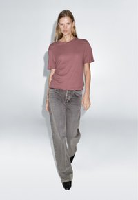 Loose-fitting maroon t-shirt made of soft fabric, paired with gray wide-leg jeans. Model wears black pointed toe heels. Simple, minimal design.