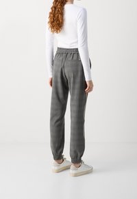 Grå rutiga joggerbyxor gjorda av mjukt tyg med elastisk midja och avskurna anklar, parat med vit långärmad topp och vita sneakers.