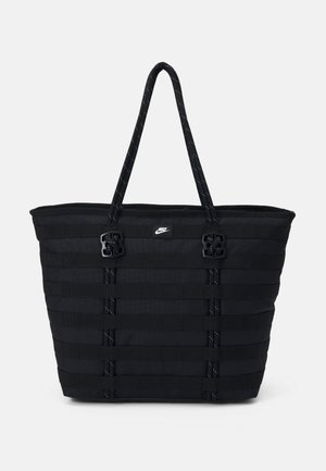 Svart nylon toteveske med horisontal webbing-design, doble håndtak og to dekorative hardware-detaljer. Lite logo på fronten.