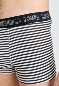 Crne i bijele prugaste bokserice s crnim pojasom na kojem se nalazi logo "KARL LAGERFELD" u bijelom vezenju. Mekan, rastezljiv materijal.