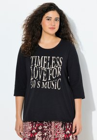Černá košile s krátkým rukávem, která má vintage styl s krémovou grafikou a nápisem "NADČASOVÁ LÁSKA K HUDBĚ 90. LET", v uvolněném střihu a se zavazováním po stranách.