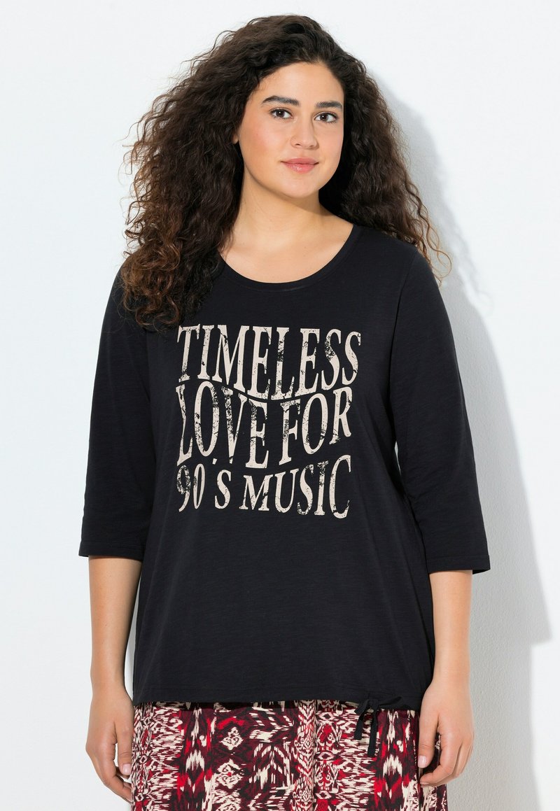 Černá košile s krátkým rukávem, která má vintage styl s krémovou grafikou a nápisem "NADČASOVÁ LÁSKA K HUDBĚ 90. LET", v uvolněném střihu a se zavazováním po stranách.