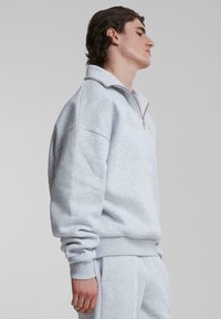 Lys grå fleece halv-zip genser med høy krage, senkede skuldre og ribbede mansjetter, med en subtil tekstur og minimalt design.