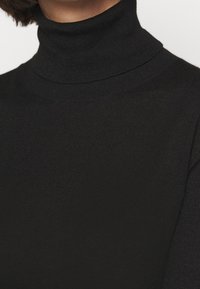 Nahaufnahme einer Person, die einen schwarzen gerippten Rollkragenpullover trägt, mit sichtbarem kurzen braunen Haar am Nacken.