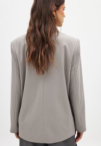 Light gray blazer featuring a smooth texture, structured shoulders, and a straight cut. Back view highlights seam details and relaxed fit.